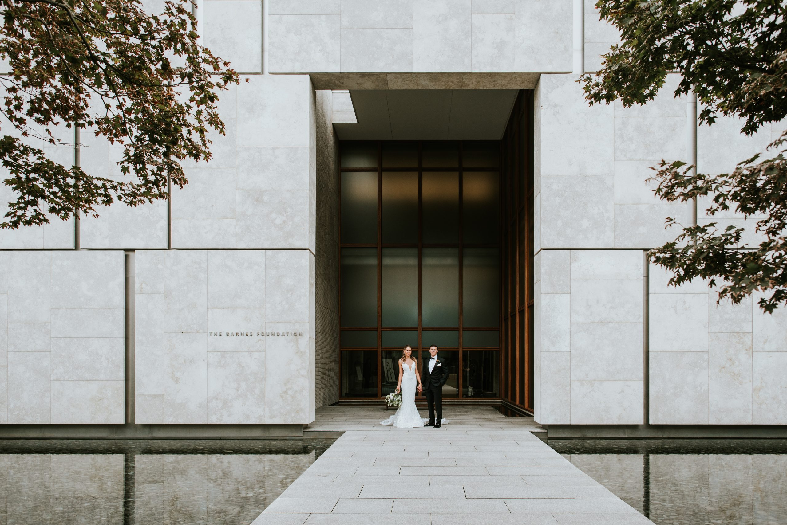 A wedding couple framed by the monumental stone entrance of the Barnes Foundation