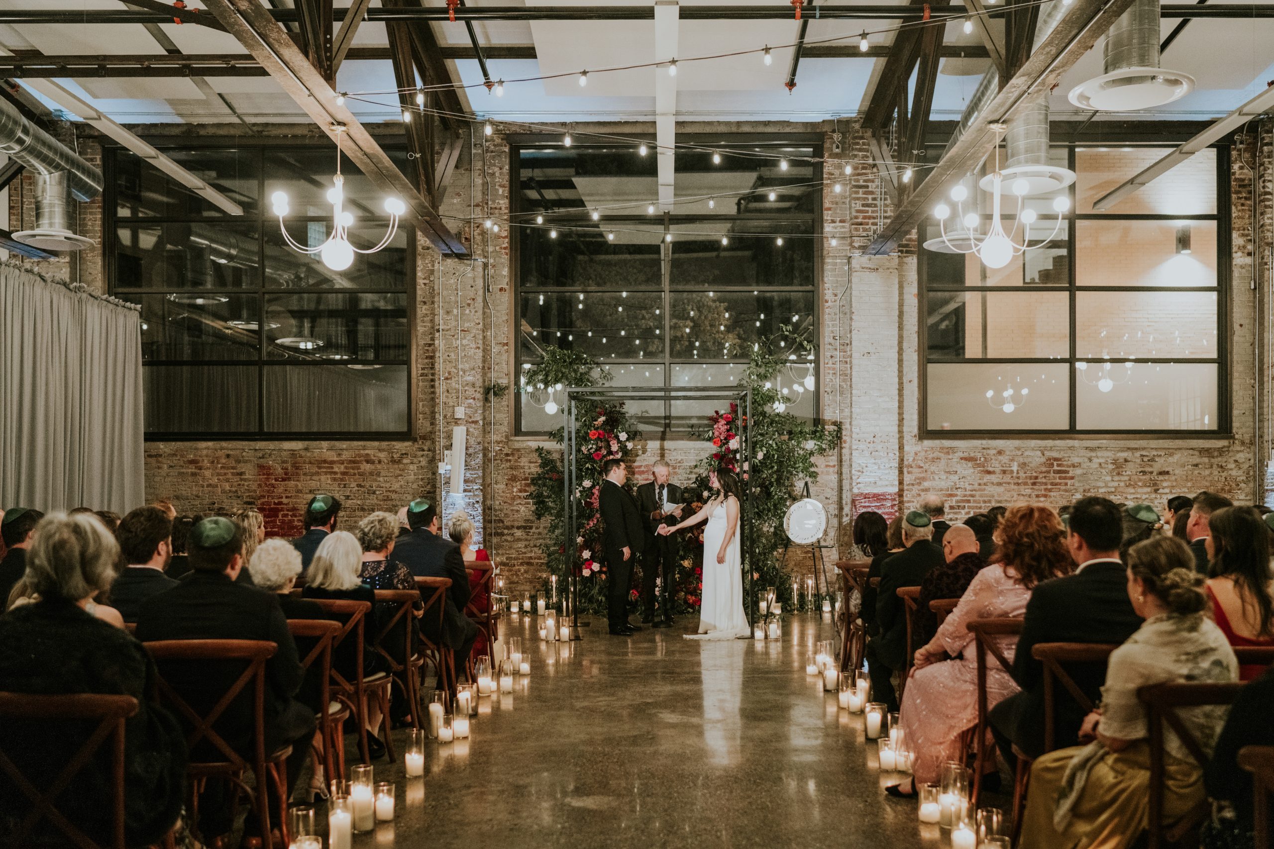 A wedding ceremony inside Lilah beneath tall windows and suspended greenery