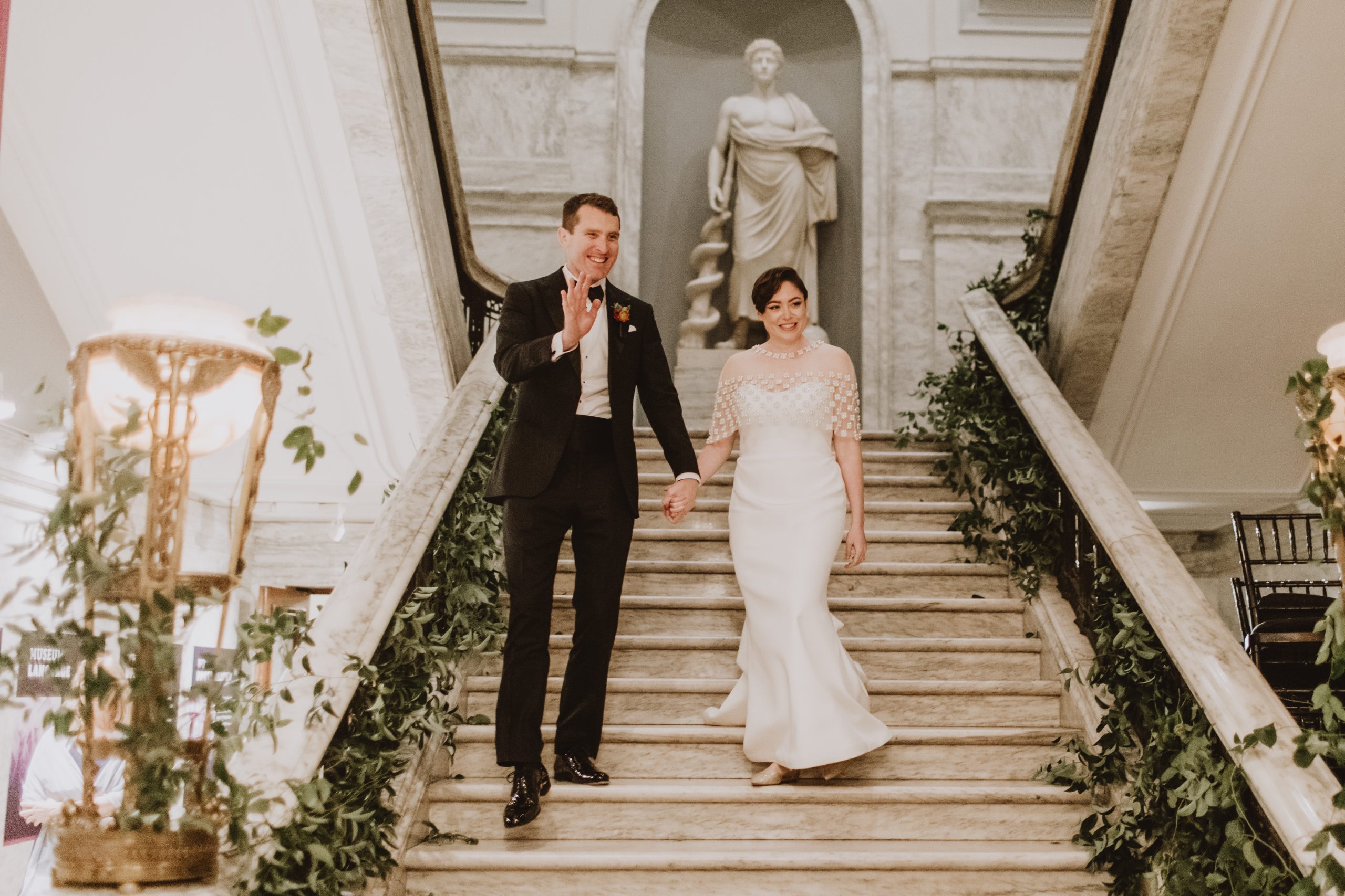 A newlywed couple descending a historic staircase beside a marble statue