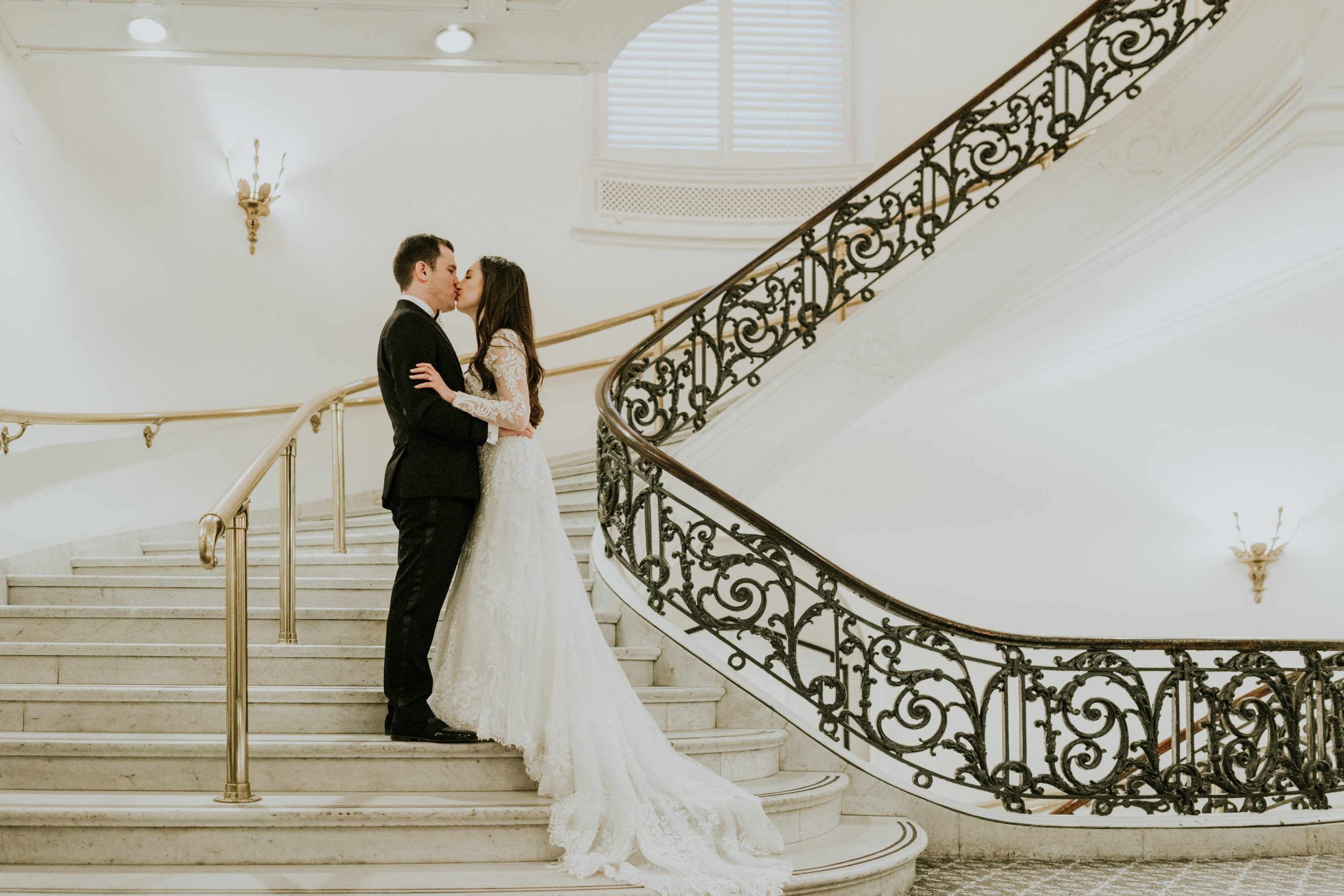 A newlywed couple kissing on a sweeping white staircase