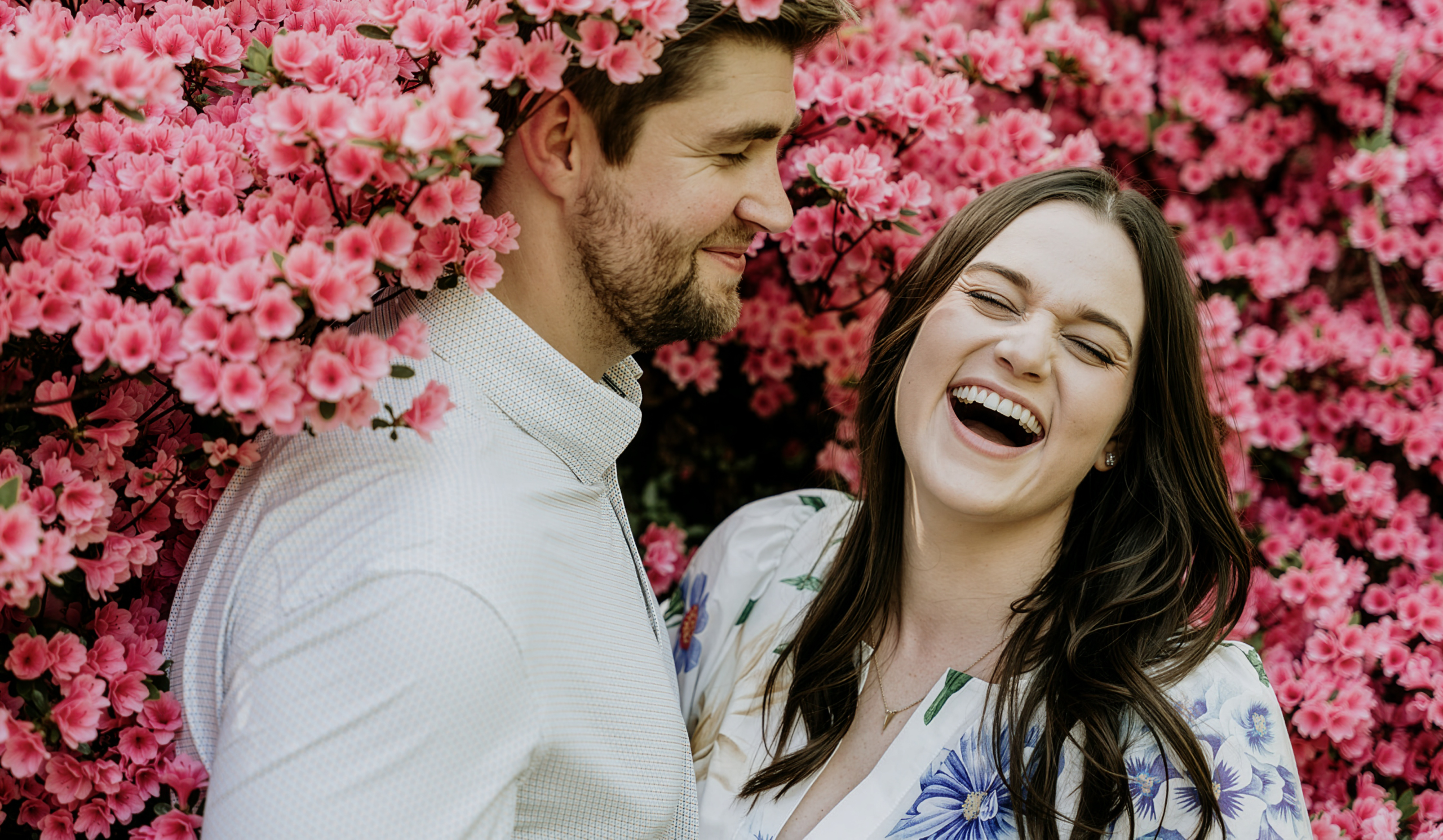 A couple laughing together among bright pink flowers